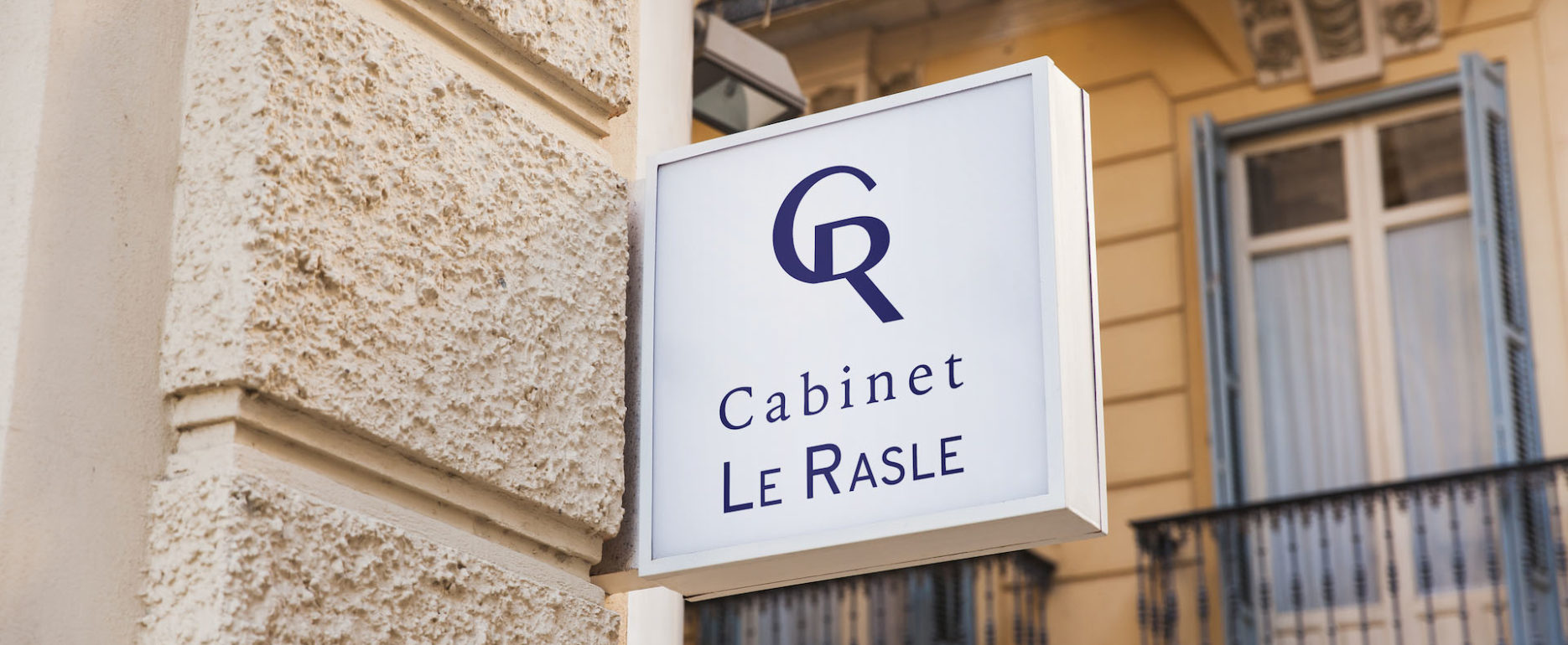 Enseigne blanche du cabinet Le Rasle accrochée sur un mur en pierres