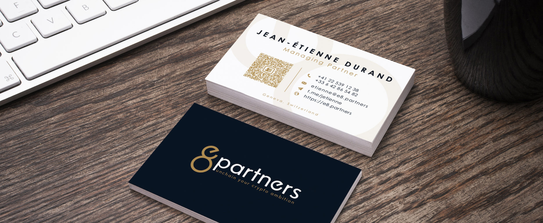 Tas de cartes de visites bleues marines et blanches posées sur un bureau devant un clavier et une tasse noire